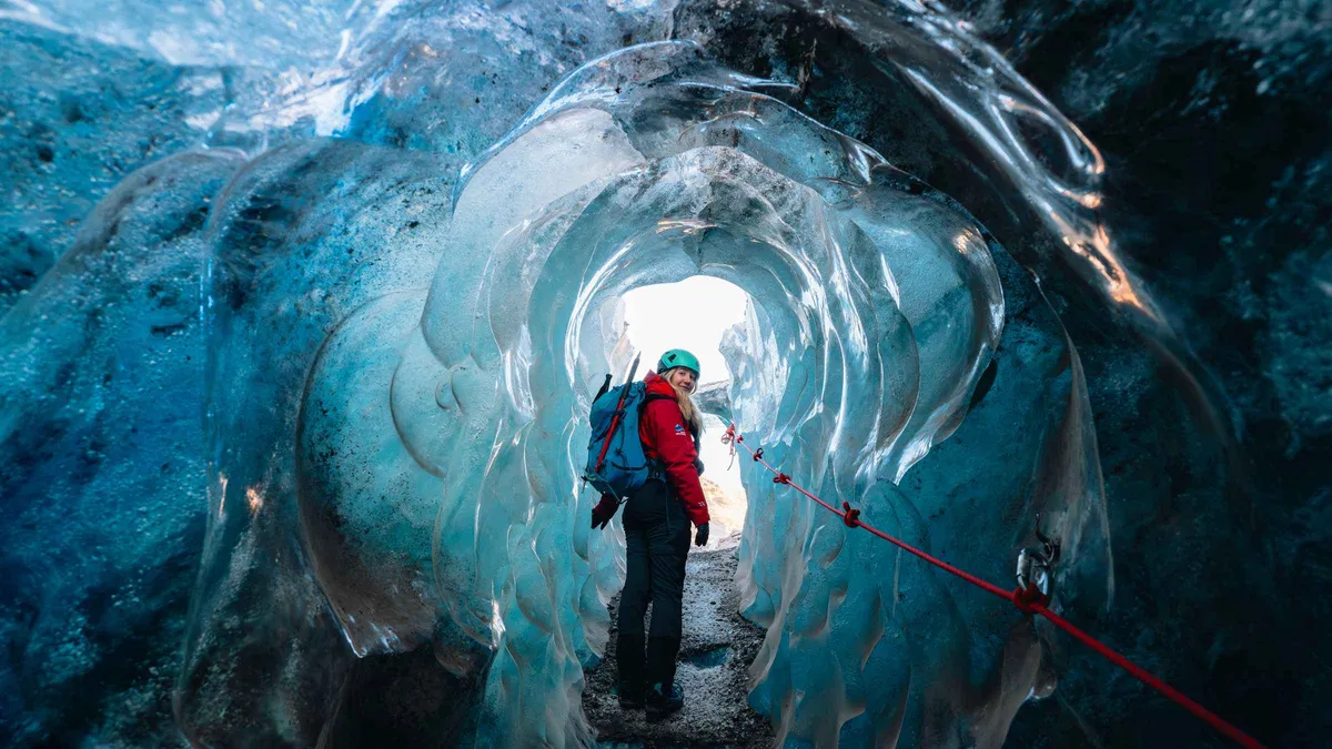 Hikers in crampons at the mouth of a blue ice cave on Falljökull during the Skaftafell Vatnajökull ice caves and glacier hike, Iceland